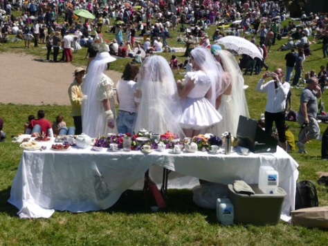 4 men dressed in bridal gowns in front of a wedding table